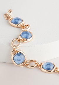 Gold-tone metal bracelet featuring blue ceramic stones set in textured, rounded links with a lobster clasp. Smooth and polished finish.