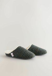 Uld slip-on hjemmesko med et struktureret mørkegrønt og gråt mønster, hvid fløjlignende foring og sorte gummisåler for godt greb.