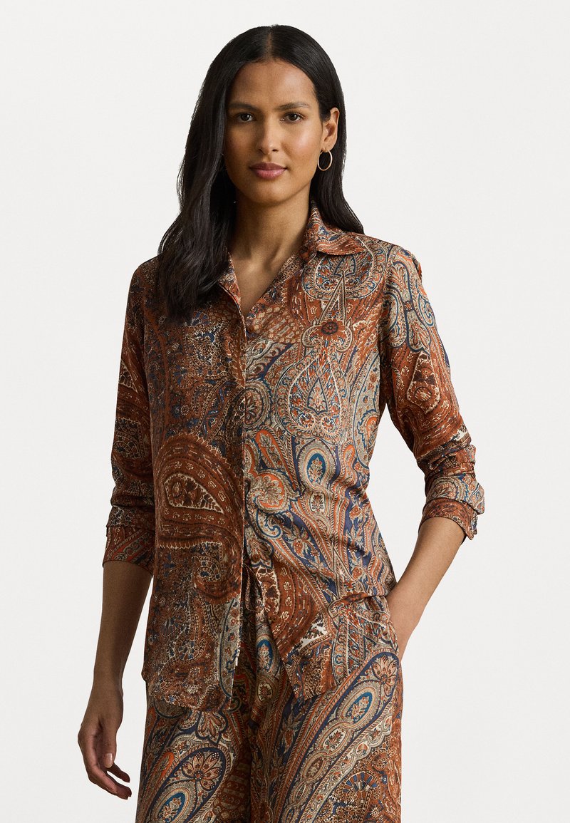 Button-up shirt made of soft fabric, featuring a paisley pattern in shades of brown, orange, blue, and cream, with roll-up sleeves.