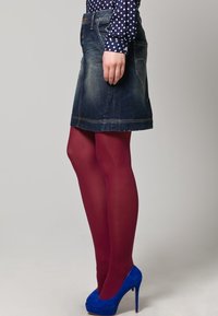 Falda de mezclilla con un diseño acampanado, combinada con medias burdeos y zapatos de tacón azul. Blusa de manga larga con lunares visible.