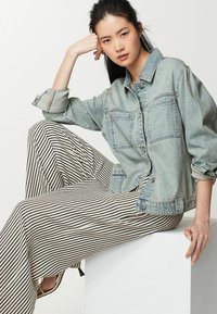 Giacca in denim azzurro chiaro con due tasche frontali, abbinata a pantaloni larghi a righe bianche e nere. Tessuti lisci, vestibilità casual.