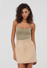 Body in verde oliva con spalline sottili abbinato a una mini gonna in denim beige chiaro con vita elastica e tasche laterali.