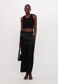Zwarte cropped tanktop, hooggeprijsde zwarte satijnen wijde broek, zwarte riem met ronde gesp, zwarte handtas, zwarte sandalen met banden.
