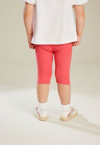 Koraalcapri leggings van zacht materiaal, met een aansluitend ontwerp en omzoomde boorden, gecombineerd met witte sneakers en enkelsokken.