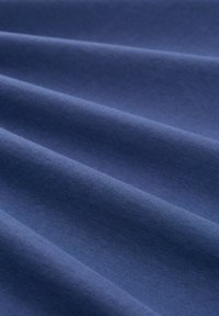 Granatowy materiał o gładkiej teksturze, ukazujący miękkie, falujące fałdy i subtelny blask od naturalnego światła. Brak widocznych wzorów lub elementów metalowych.