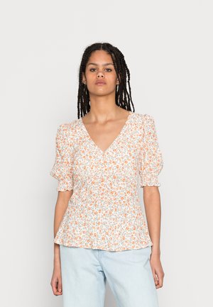 Blusa floral com mangas curtas franzidas, fundo branco, flores laranjas, design em V e cintura peplum. Acompanhada de calças azul claro.