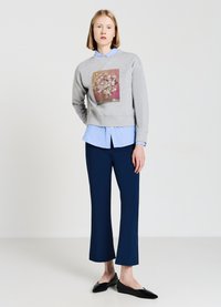 Felpa grigia con stampa floreale, indossata sopra una camicia azzurro chiaro. Pantaloni navy con taglio dritto e ballerine nere a punta.