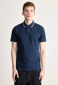 Tricou polo albastru marin din bumbac, cu m�âneci scurte și margine albă, cu două nasturi și un mic patch cu logo pe piept.