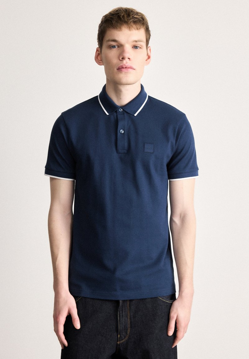 Tricou polo albastru marin din bumbac, cu mâneci scurte și margine albă, cu două nasturi și un mic patch cu logo pe piept.