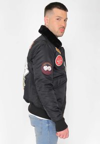 Svart bomberjacka med krage av konstfuskpäls, broderade lappar och ribbade ärmslut. Har dragkedjestängning och en figurnära design.