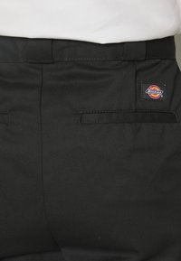 Sorte arbeidsbukser laget av slitesterkt stoff, med en baklomme med brodert Dickies-logo og flat, forsterket søm.