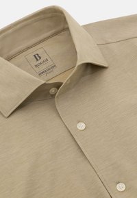 Camisa beige de botones con cuello clásico, textura suave y una etiqueta que dice "BOGGI JAPANESE EXCLUSIVE" debajo del cuello.