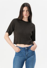 Brun ribbad kortärmad tröja med en kort design. Matchad med blå högmidjade jeans. Slät textur, minimalistisk stil.