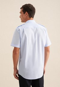Camicetta a maniche corte in tessuto blu chiaro con una texture liscia, caratterizzata da un colletto dritto e accenti blu a contrasto sulle spalle.