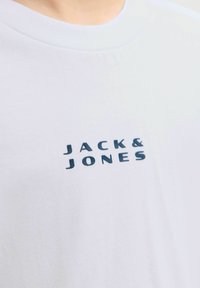 Valge lühikeste varrukatega t-särk, mis on valmistatud pehmest puuvillast, millel rinnal on tume sinine "JACK & JONES" logo. Sile tekstuur, jaane disain.