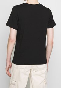 Camiseta negra de manga corta, con cuello redondo, material de algodón, textura suave, diseño simple, sin patrones ni gráficos visibles, corte estándar.