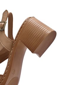 Sandal in pelle marrone con tacco a blocco largo e texture. Dotata di una fascia regolabile con fibbia e cuciture visibili lungo la suola.