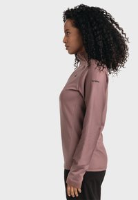 Enganliegendes, langärmliges Oberteil in hellem Mauve mit hohem Kragen. Verfügt über eine dezente gerippte Textur und Branding am linken Ärmel.