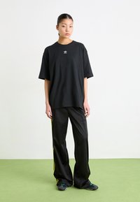 Black oversized cotton t-shirt with a small white logo on the chest, paired with black wide-leg pants featuring yellow side stripes.