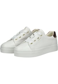 Sneaker bianche in pelle con suola strutturata, occhielli dorati e un accento metallico sul tallone. Presentano lacci piatti e punta arrotondata.