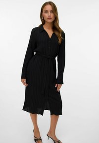 Abito camicia nero a maniche lunghe con strisce verticali, apertura a bottoni sul davanti e cintura in vita. Tessuto morbido con vestibilità leggermente rilassata.