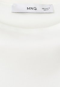 Weißer Kleidungsstück-Ausschnitt mit einem Etikett, auf dem "MNG" steht, sowie Größenangaben EUR S, USA 4, MEX CH.