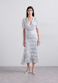 Light gray, tiered midi dress with a deep V-neck, textured fabric, short puff sleeves, and shimmering finish, complemented by silver heels.