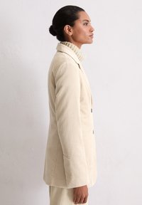 Beige corduroy blazer met een geknipt kraag, een enkel knoopsluiting ontwerp en een textuurstof. Voorzien van twee knopen en zijzakken.