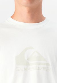 T-shirt de algodão branca com um logótipo Quiksilver verde claro na frente. Design clássico de gola redonda com mangas curtas.