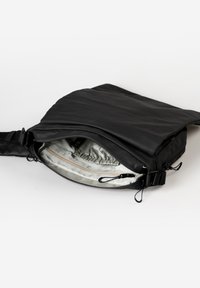 Schwarze, weiche Stofftasche mit verstellbarem Tragegurt; weiter Öffnung zeigt ein helles Innenfutter und eine Reißverschlusstasche. Glatte Textur, elegantes Design.
