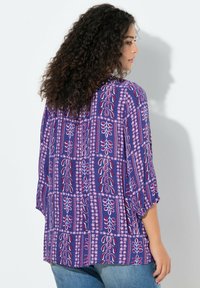 Kolorowa bluzka w odcieniach fioletu z kwiatowymi i geometrycznymi wzorami. Charakteryzuje się luźnym, swobodnym krojem i rękawami o długości do łokcia. Gładka tekstura tkaniny.