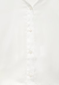 Blouse blanche à texture lisse avec cinq boutons en perle le long de la patte de boutonnage avant et un décolleté en V.