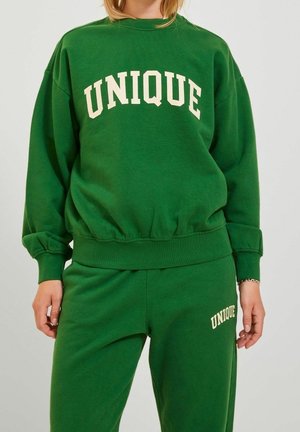 Grüner Sweatshirt mit "UNIQUE" in Creme gedruckt, mit geripptem Saum und Bündchen, kombiniert mit passenden grünen Sweatpants, ebenfalls mit "UNIQUE"-Details.