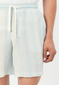 Pantalones cortos de textura de gofre en blanco y azul claro, con cintura elástica y cordón ajustable. Largo hasta el muslo.