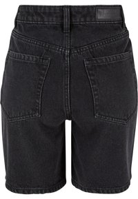 Short en denim noir vu de dos avec deux grandes poches carrées et une étiquette en cuir brandée sur la ceinture.