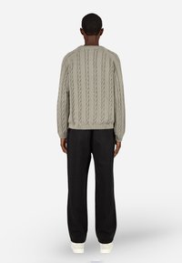 Pulover v svetlo sivi pleteni strukturi z rebrastim robom, v kombinaciji z črnimi širokimi hlačami in belimi supergami. Nevtralni toni in teksturirana zasnova.