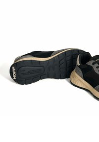 Zapatillas atléticas en negro y gris que cuentan con una suela de goma texturizada, parte superior de gamuza y malla, mediasuela acolchada y detalle del logo en el talón.