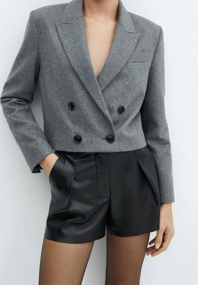 Blazer court croisé gris en tissu texturé, avec des boutons noirs et des revers ajustés, associé à un short en cuir noir.