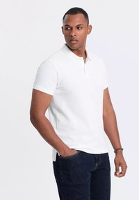 Polo blanca de algodón, con un cuello clásico y mangas cortas. Combinada con jeans azul oscuro, resalta la simplicidad y la comodidad.