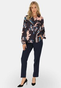 Kwiatowa bluzka z długim rękawem w ciemnym materiale z różowymi i niebieskimi wzorami, zestawiona z granatowymi spodniami slim fit i czarnymi szpilkami.