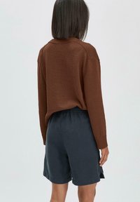 Pull en tricot marron à manches longues, associé à un short bleu foncé. Le pull a une coupe décontractée et des poignets côtelés.