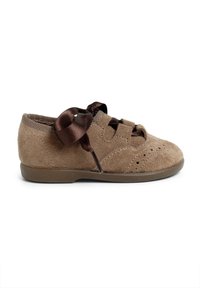 Zapato de ante marrón con suela plana, que presenta una superficie texturizada, perforaciones decorativas y un lazo de cinta de satén en un lado.
