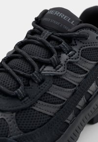Svarte joggesko med mesh og syntetiske overlegg, med teksturerte snøringer og forsterket hæl for støtte. Merking synlig på tungen.