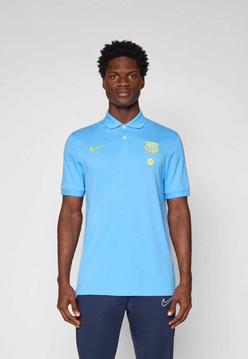 Svjetloplava pamučna polo majica. Ima ovratnik, kratke rukave, Nike logo u žutoj boji i grb Barcelone na lijevoj strani prsa.