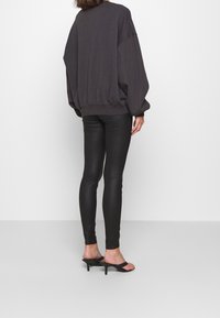 Överdimensionerad mörkgrå sweatshirt med ribbad nederkant, matchad med tajta svarta leggings och svarta klacksandaler. Slät tygtextur.