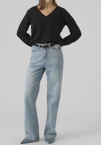 Maglione nero con texture e scollo a V, abbinato a jeans larghi di colore blu chiaro. Presenta una cintura nera e tacchi blu appuntiti.