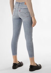 Ljust blå stretchjeans med hög midja och bakfickor, med en distinkt sömdesign. Kombinerat med svarta skor.