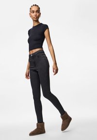 Μαύρη εφαρμοστή μπλούζα, ψηλόμεσα μαύρα skinny τζιν και καφέ μπότες μέχρι τον αστράγαλο. Λείο ύφασμα, απλός σχεδιασμός και μαλακή υφή.