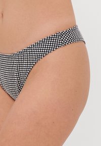 Bas de bikini à carreaux noir et blanc en matériau élastique. Doté d'une taille étroite et d'un design à couverture minimale.