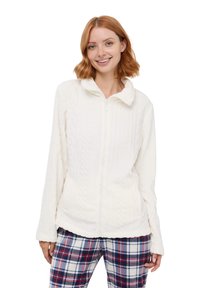 Giacca in pile bianca con zip, design a maglia a trecce testurizzate, tessuto morbido e colletto. Abbinata a pantaloni scozzesi nei toni di rosso, blu e bianco.